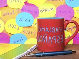 A coffee mug on a desk that says "Hablamos espanol".