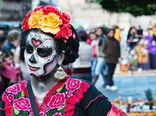 A person wearing day of the dead sugar skull make-up, a flower headband, and traditional spanish dress.